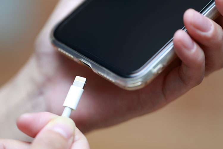 充電のためiPhoneにライトニングケーブルを刺そうとしている手の画像