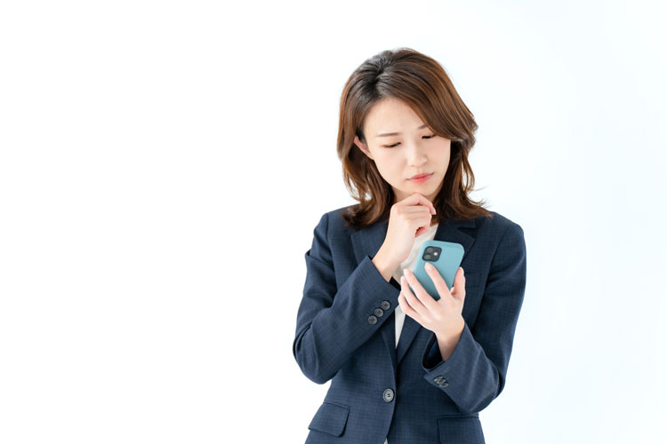 iPhoneを見ながら顎に手を当てて悩んでいる女性